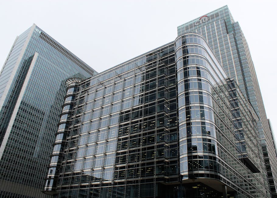 A black and white photograph of the exterior of a modern commercial building with a curved glass facade, featuring multiple horizontal and vertical lines created by the window frames and structural el